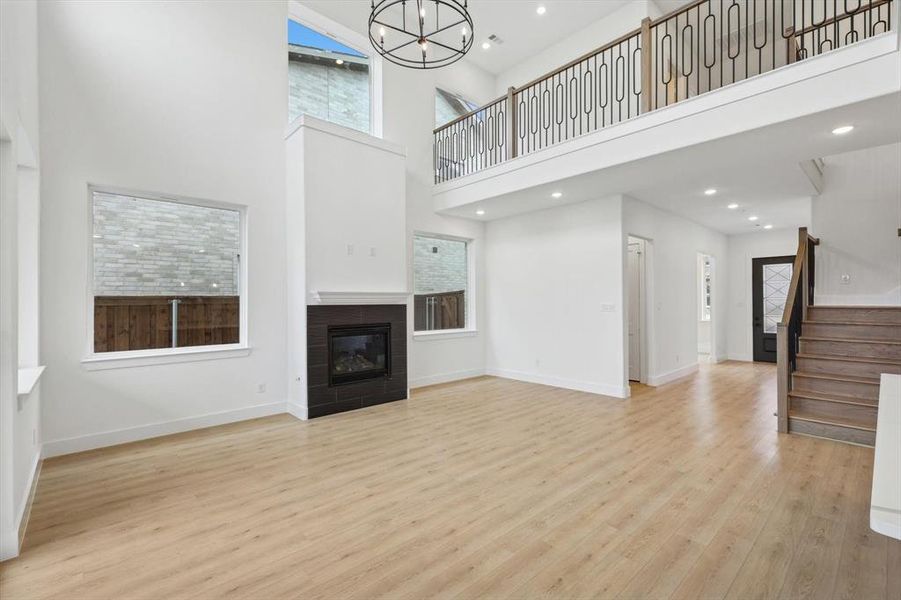 Unfurnished living room with a tiled fireplace, a towering ceiling, light hardwood / wood-style flooring, and an inviting chandelier