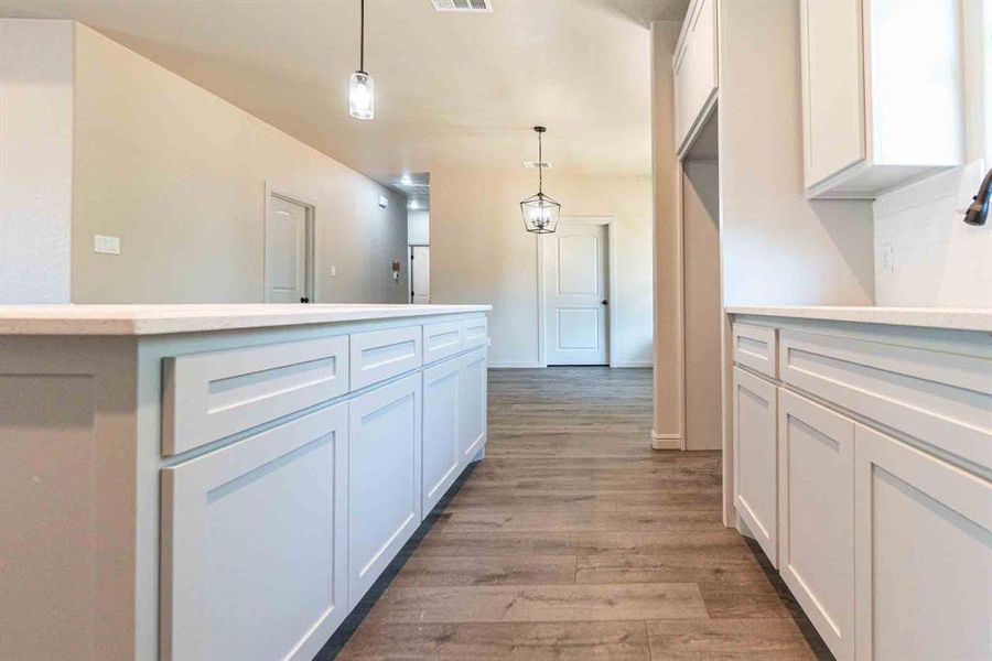 Kitchen featuring light wood-style floors, pendant lighting, backsplash, white cabinets, and a center island