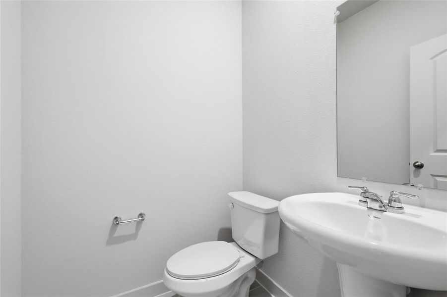 Bathroom featuring a pedestal sink with chrome faucet, a white toilet, and a wall-mounted mirror