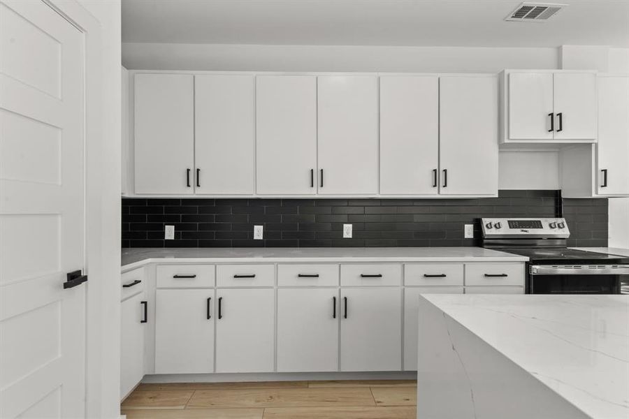 Kitchen featuring stainless steel electric stove, visible vents, decorative backsplash, light wood-style floors, and white cabinets