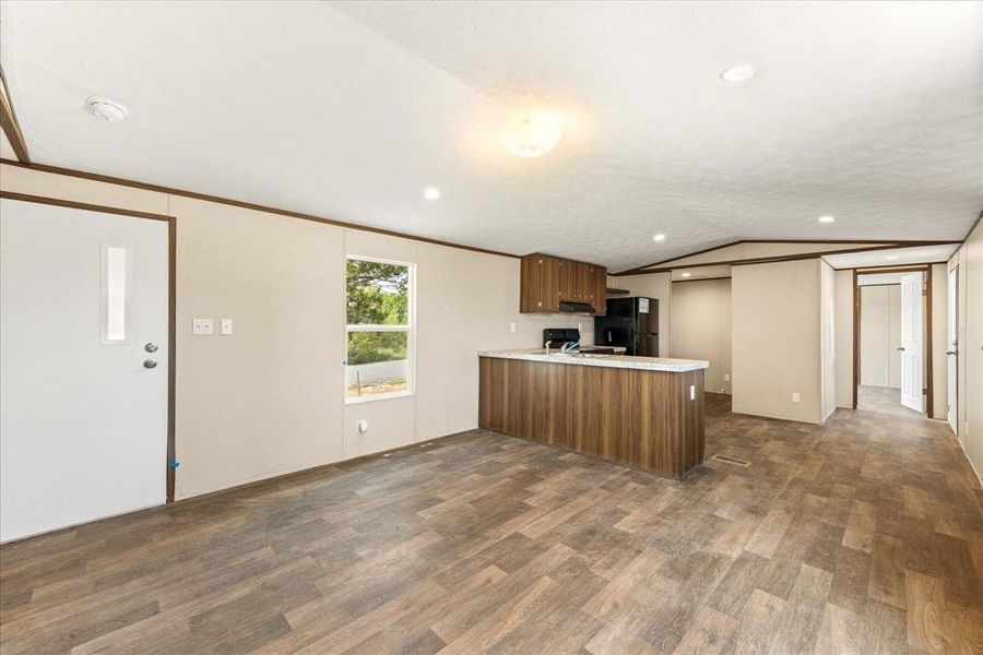 Open-concept living area featuring wood-finish flooring, a kitchen island with a light-toned countertop, dark wood cabinetry, and recessed lighting