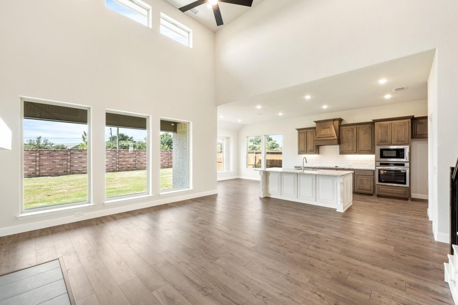 Open living area with high ceilings and hardwood floors flowing into kitchen with white island and dark wood cabinets