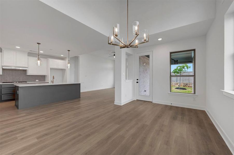 Open concept living space featuring wide plank flooring, a contemporary chandelier, a kitchen island with pendant lighting, and a window providing views of the outdoor space