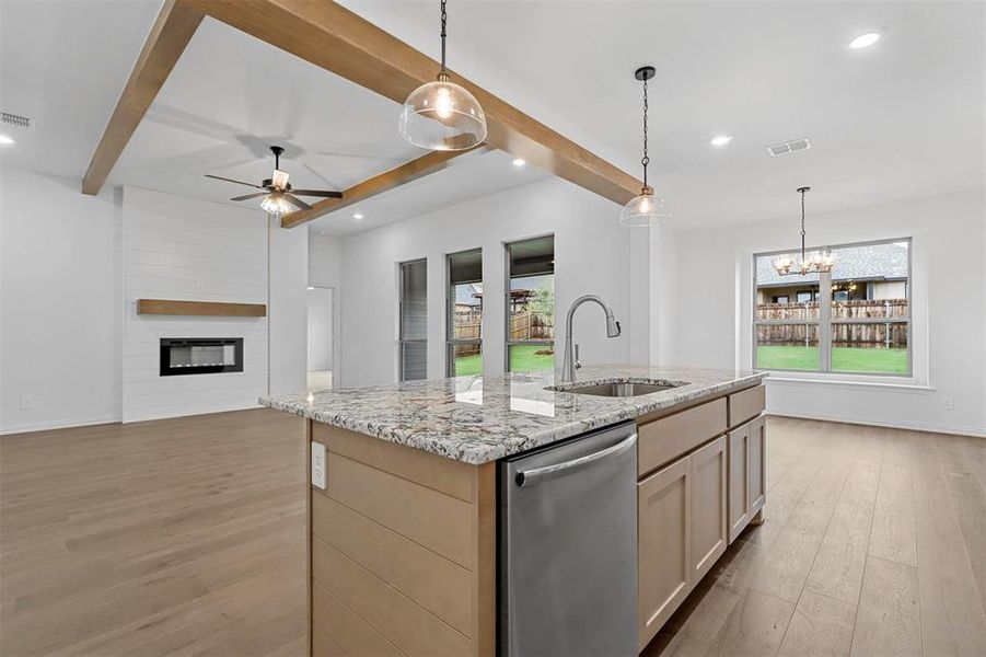 Kitchen with light stone counters, an island with sink, stainless steel dishwasher, a fireplace, and light wood-type flooring