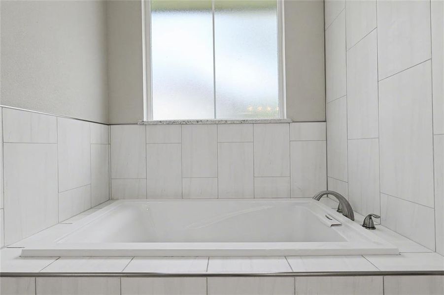 Built-in soaking tub with brushed nickel fixtures, surrounded by white rectangular tile and a privacy window with a granite sill