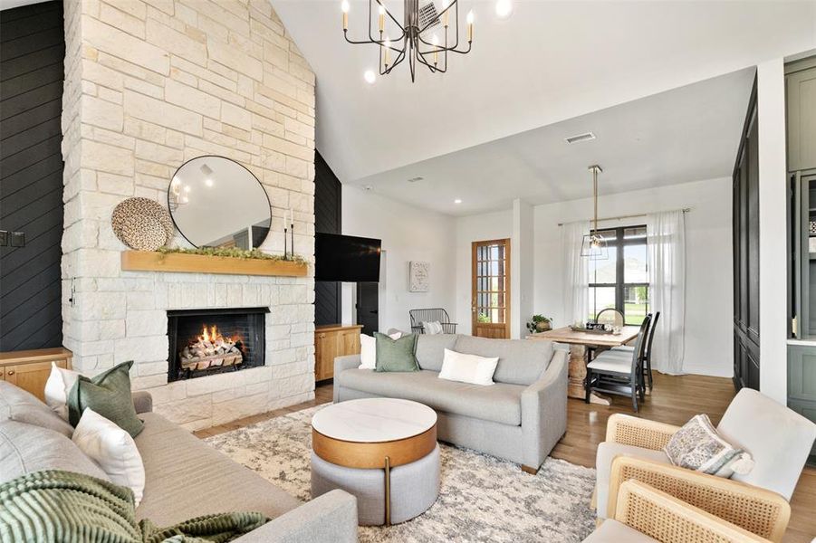 Living room with wood finished floors, a chandelier, a fireplace, recessed lighting, and high vaulted ceiling