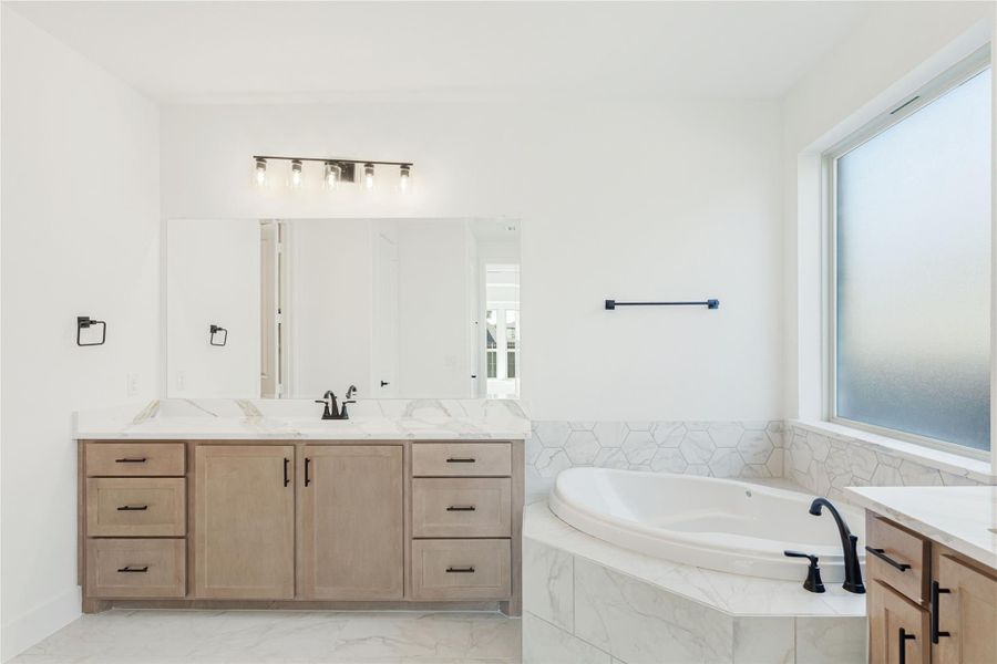 Master bathroom with wood vanity, marble countertop, soaking tub, and geometric tile surround