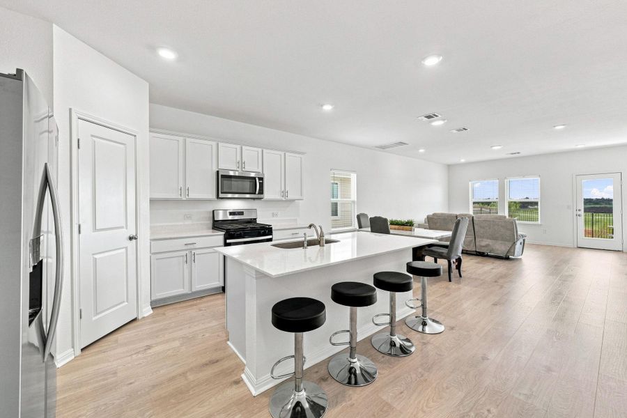 Recessed lighting illuminates this bright, open kitchen featuring a central island and light wood floors.