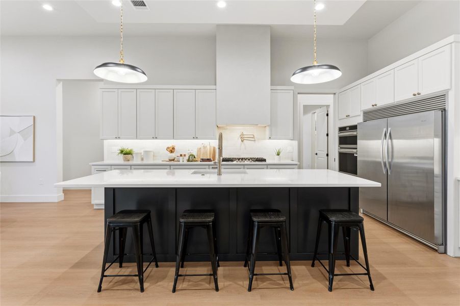 Kitchen featuring white cabinetry, stainless steel appliances, a kitchen bar, a center island with sink, and decorative light fixtures