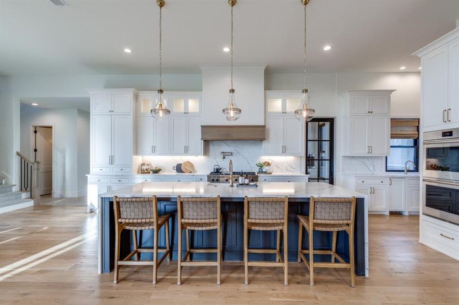 Kitchen featuring a kitchen island with sink, white cabinets, double oven, tasteful backsplash, and recessed lighting Kitchen featuring a kitchen island with sink, white cabinets, double oven, tasteful backsplash, and recessed lighting
