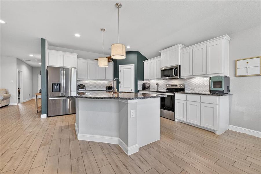 Modern kitchen featuring white shaker cabinetry, stainless steel appliances, speckled countertops, a hexagon tile backsplash, and wood-finish flooring