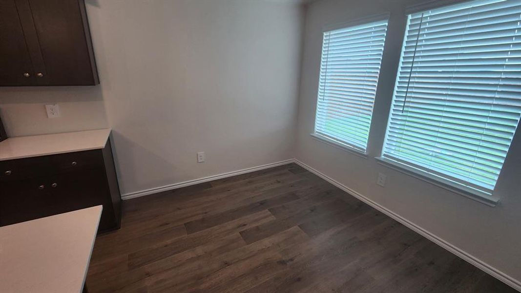Breakfast nook featuring two windows with horizontal blinds, dark wood-finish flooring, white baseboards, and a white wall finish Breakfast nook featuring two windows with horizontal blinds, dark wood-finish flooring, white baseboards, and a white wall finish