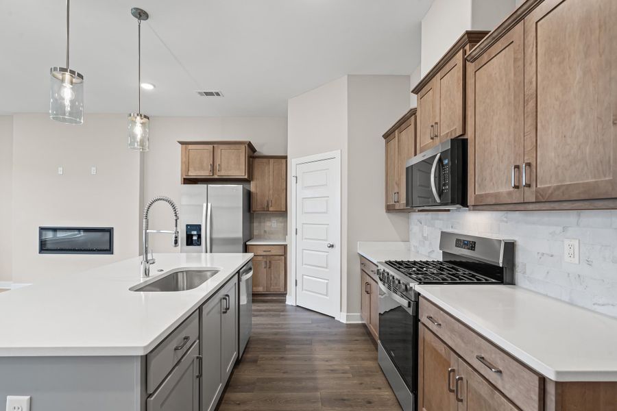 Kitchen with appliances with stainless steel finishes, pendant lighting, decorative backsplash, dark wood-style flooring, and a kitchen island with sink