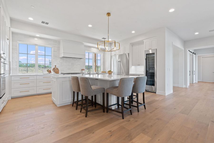 Kitchen featuring a center island with sink, light wood finished floors, premium range hood, and stainless steel appliances Kitchen featuring a center island with sink, light wood finished floors, premium range hood, and stainless steel appliances