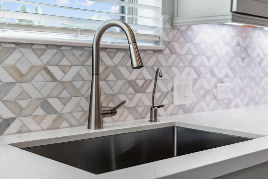 This kitchen features a sleek, spot-free stainless steel pull-down faucet and a modern double-basin sink, set against a striking gray and white chevron mosaic backsplash. This kitchen features a sleek, spot-free stainless steel pull-down faucet and a modern double-basin sink, set against a striking gray and white chevron mosaic backsplash.