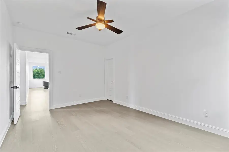 Spacious room featuring light wood-finish flooring, a contemporary ceiling fan with integrated lighting, and crisp white walls