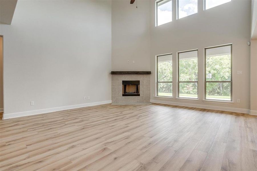 Unfurnished living room with light hardwood / wood-style floors, a tiled fireplace, ceiling fan, and a high ceiling