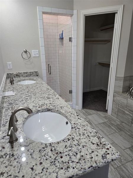 Bathroom featuring dual bowl vanity, tile floors, and a shower with door