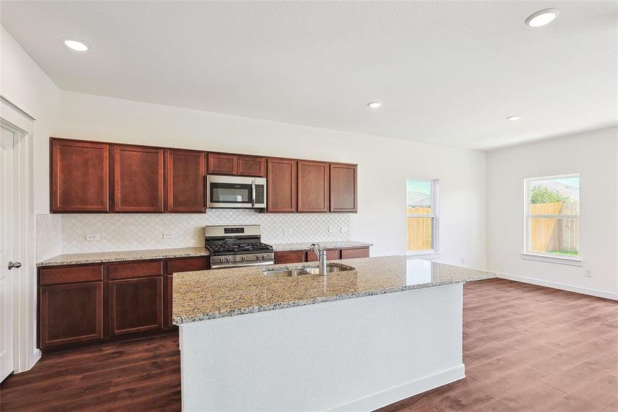 Kitchen with stainless steel appliances, dark wood-style floors, light stone countertops, a center island with sink, and recessed lighting