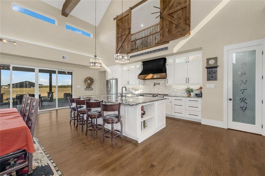 Kitchen featuring white cabinetry, glass insert cabinets, backsplash, high vaulted ceiling, and a kitchen bar