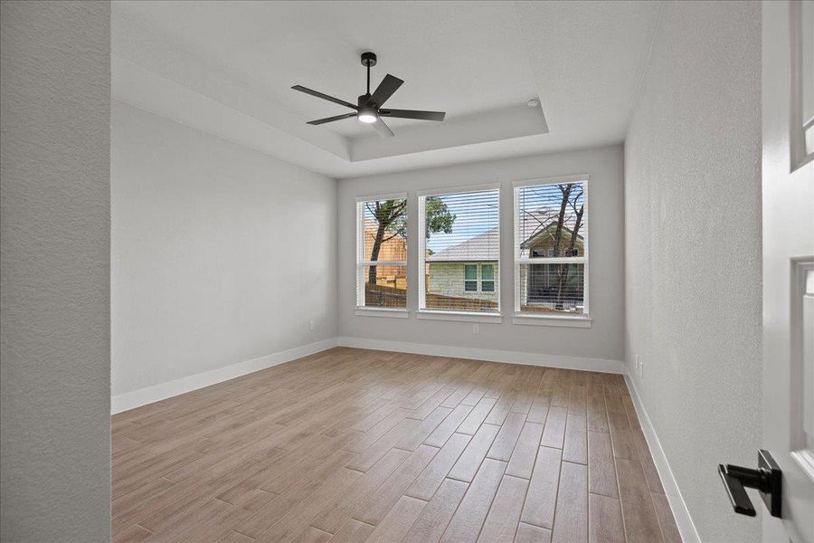Spare room featuring a tray ceiling, a textured wall, light wood-style floors, and a ceiling fan Spare room featuring a tray ceiling, a textured wall, light wood-style floors, and a ceiling fan
