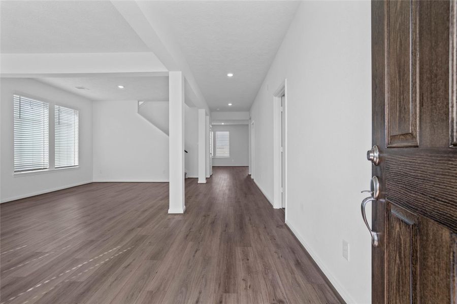 Welcome home to this bright and airy open-concept layout, featuring durable luxury vinyl plank flooring and crisp white walls that maximize natural light. The expansive space seamlessly transitions from an inviting formal living and dining area into the rest of the home, framed by elegant structural pillars and modern recessed lighting. Perfect for entertaining, this versatile floor plan offers a clean, contemporary canvas ready for your personal touch.
