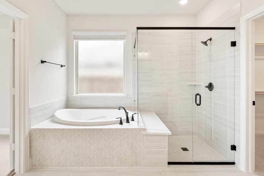 Master bathroom with soaking tub, herringbone tile surround, and glass walk-in shower with black fixtures