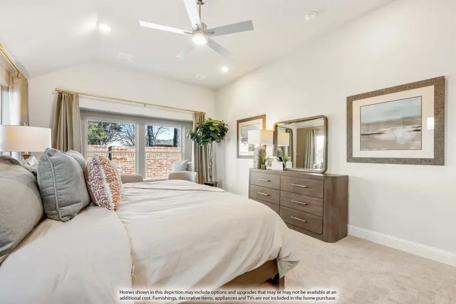 Bedroom with vaulted ceiling, ceiling fan, wood dresser, and large window with neutral carpet and bedding