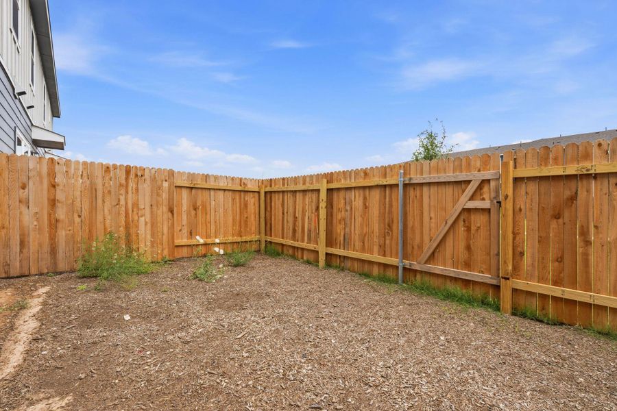 Private backyard featuring a wood privacy fence with a scalloped top and a functional gate Private backyard featuring a wood privacy fence with a scalloped top and a functional gate