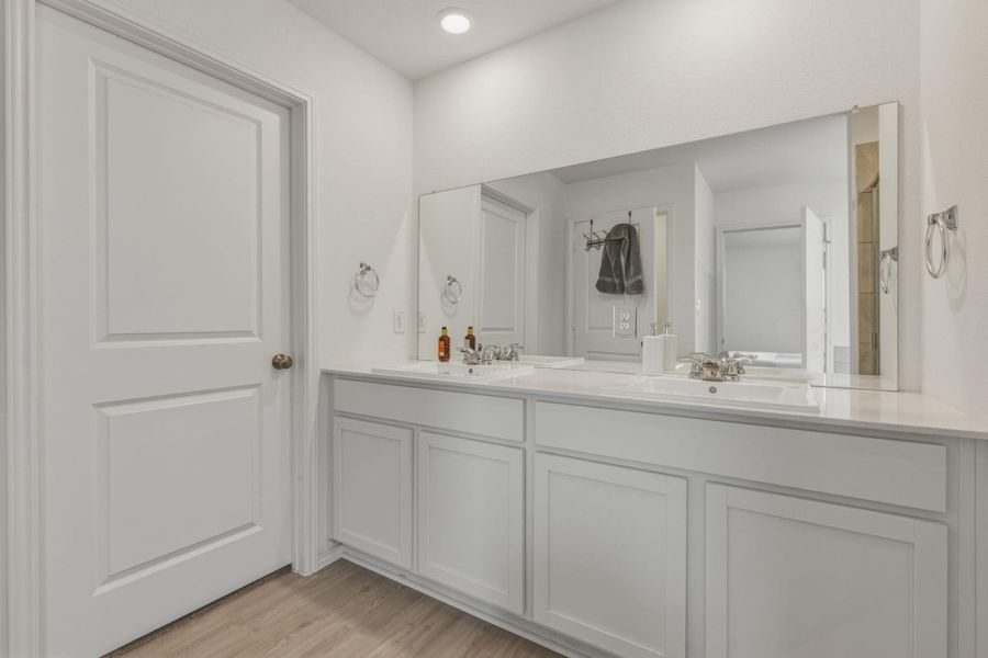 Bathroom with a long vanity featuring two sinks, white cabinetry, and a large mirror