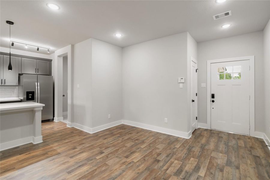 This photo shows a modern entryway with light gray walls and wood-style flooring. The space features recessed lighting, a white front door with glass panes, and an open view into a kitchen area with stainless steel appliances and gray cabinetry. This photo shows a modern entryway with light gray walls and wood-style flooring. The space features recessed lighting, a white front door with glass panes, and an open view into a kitchen area with stainless steel appliances and gray cabinetry.