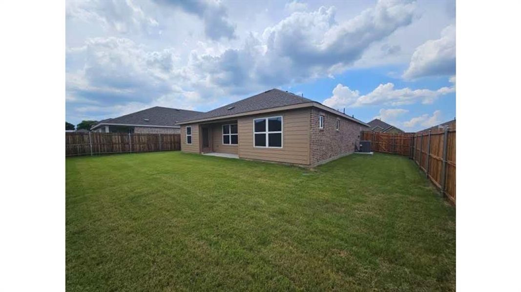 Expansive backyard featuring a manicured lawn, full perimeter wood fencing, a brick and siding exterior, and a covered concrete patio Expansive backyard featuring a manicured lawn, full perimeter wood fencing, a brick and siding exterior, and a covered concrete patio