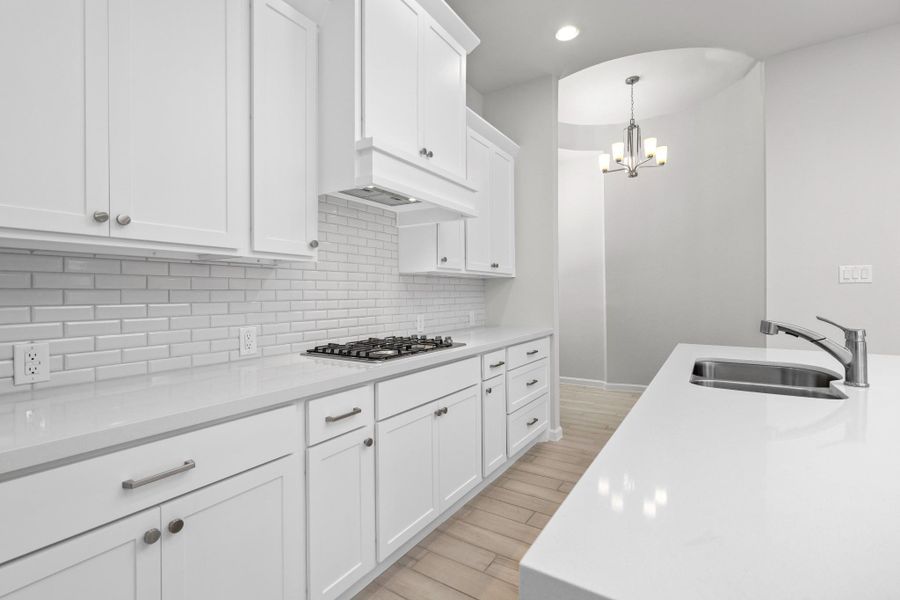 White kitchen with gas cooktop, tile backsplash, abundant cabinetry and counter space.