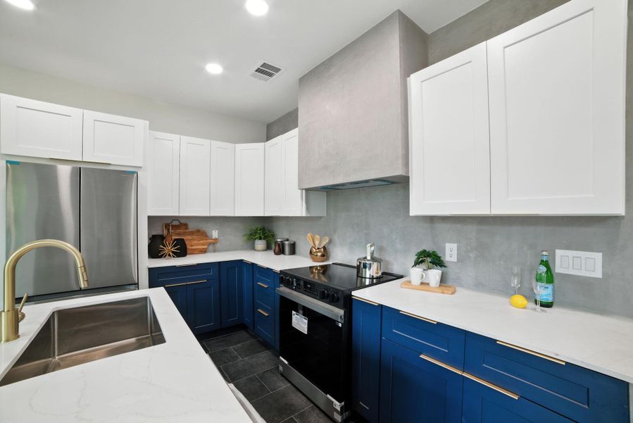 Kitchen with blue cabinetry, black range with electric stovetop, freestanding refrigerator, white cabinets, and light stone countertops Kitchen with blue cabinetry, black range with electric stovetop, freestanding refrigerator, white cabinets, and light stone countertops