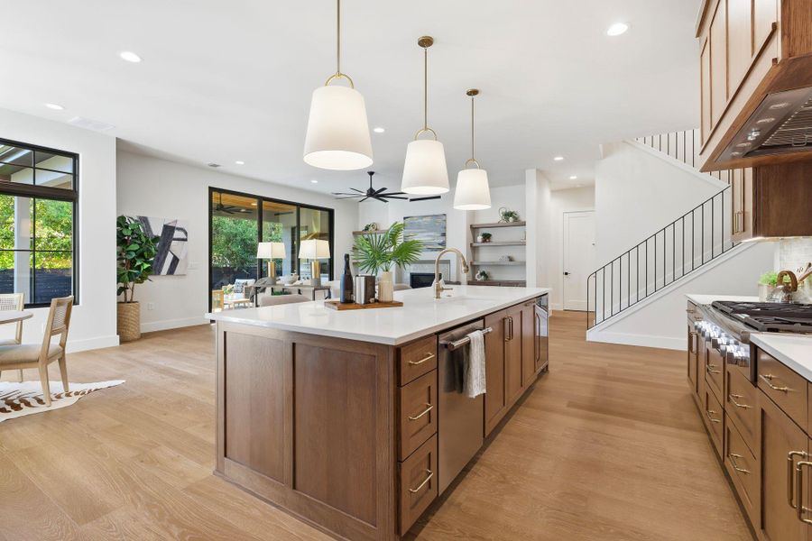 Kitchen with light wood-type flooring, brown cabinetry, decorative light fixtures, under cabinet range hood, and recessed lighting