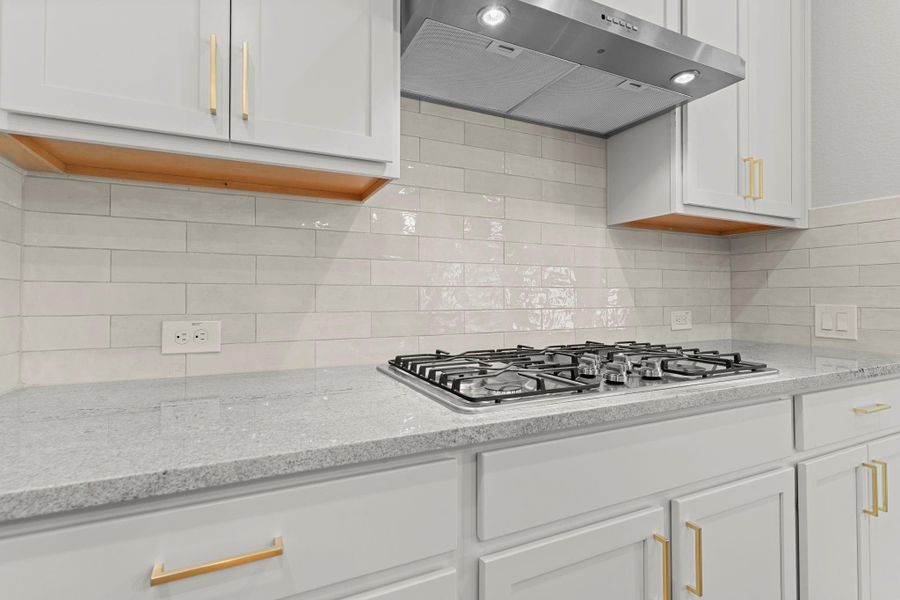 A closer look at the kitchen showcases the 5-burner gas cooktop with modern vent hood, stylish tile backsplash, and gold-tone hardware for a polished, designer-inspired look. A closer look at the kitchen showcases the 5-burner gas cooktop with modern vent hood, stylish tile backsplash, and gold-tone hardware for a polished, designer-inspired look.