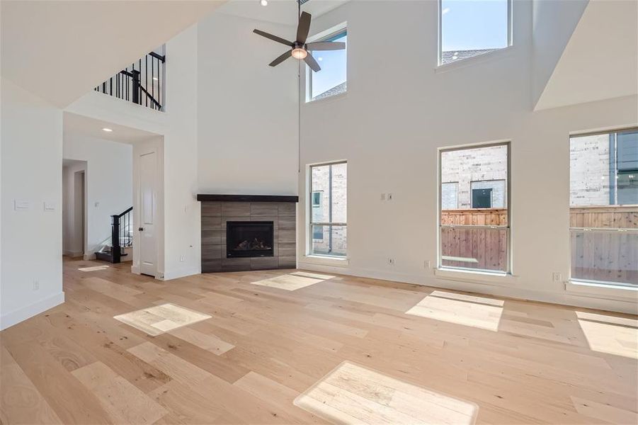 Unfurnished living room featuring a fireplace, ceiling fan, light hardwood / wood-style floors, and a towering ceiling