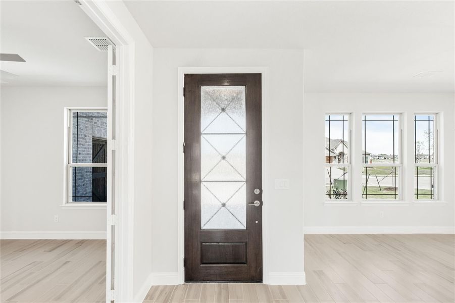 Entryway with dark wood front door featuring decorative glass panel and light hardwood floors Entryway with dark wood front door featuring decorative glass panel and light hardwood floors