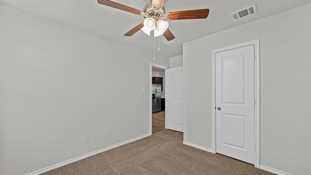 Unfurnished bedroom with stainless steel fridge, dark colored carpet, and a ceiling fan