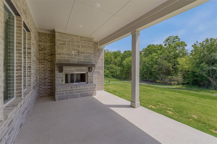 Covered patio featuring an outdoor stone fireplace with a dark wood mantle, light brick exterior, and a concrete surface