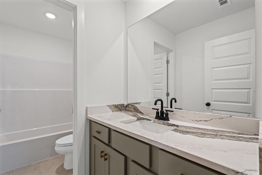 Undermount sink with a black-finish faucet, stone-finish countertop, gray cabinetry, and a full-width mirror