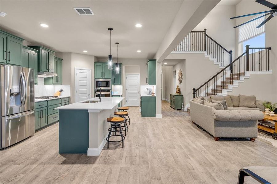 Kitchen featuring green cabinets, stainless steel appliances, a kitchen bar, open floor plan, and hanging light fixtures