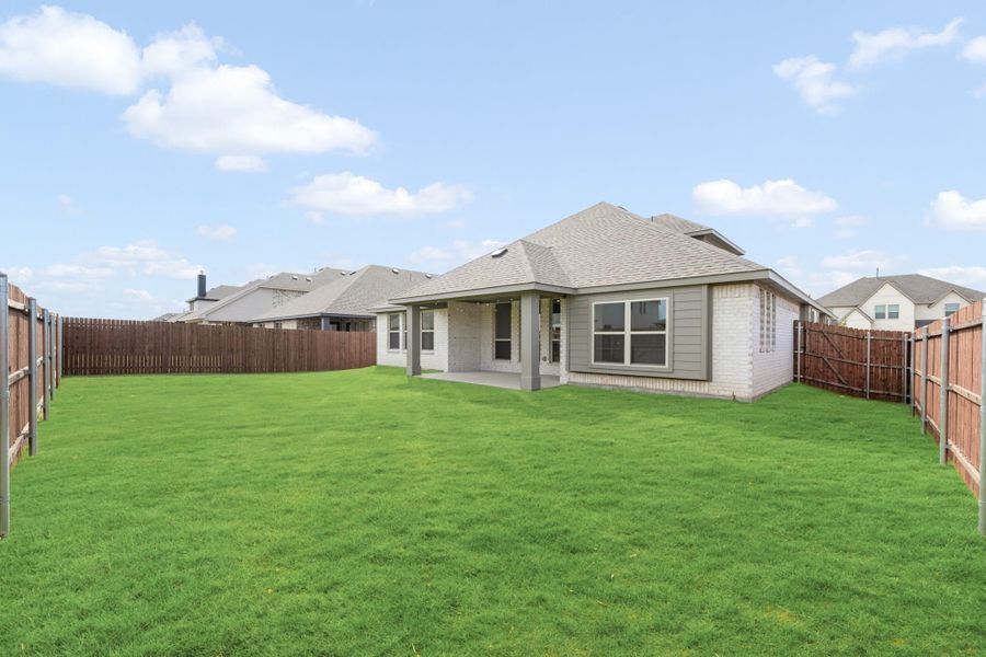 Backyard of single-story home with large green lawn, covered patio, and wood privacy fence