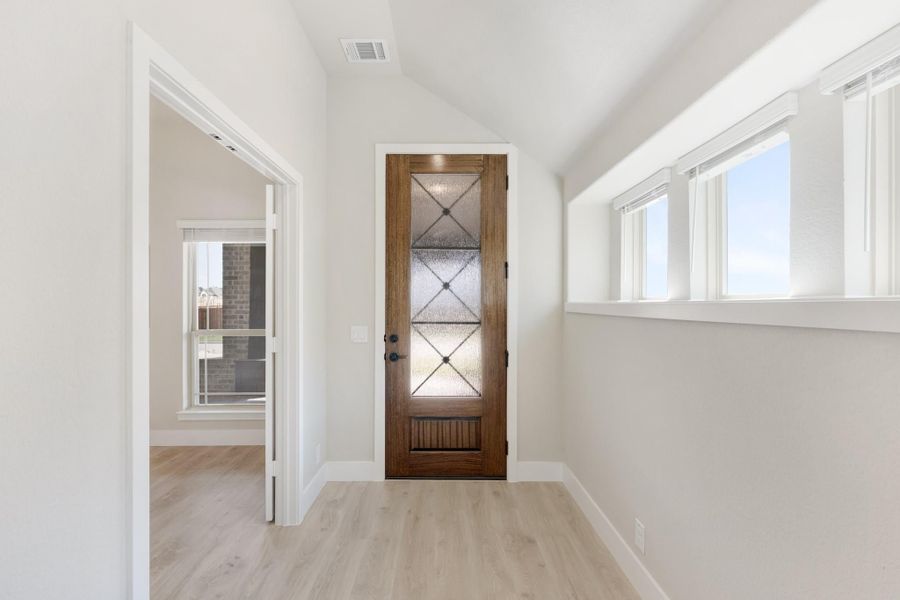 Entryway with wood door featuring decorative glass panels, vaulted ceiling, and light hardwood floors