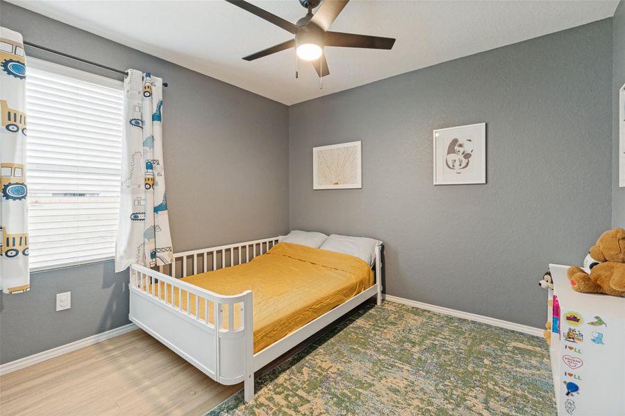 A well-lit bedroom features hardwood flooring and a ceiling fan for comfort.