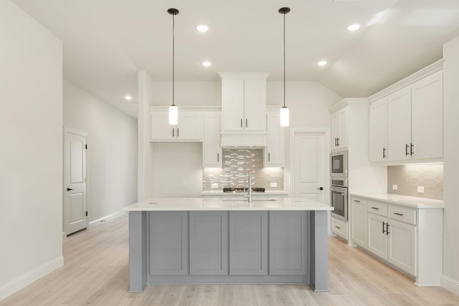 Kitchen with white cabinets, gray island, pendant lights, and light wood floors