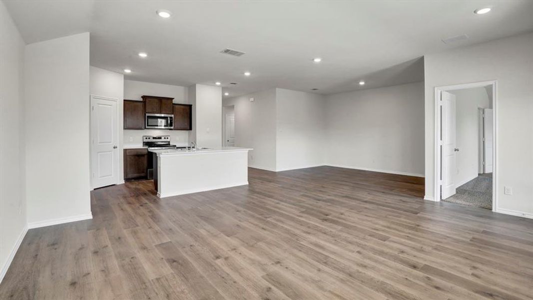 Expansive open-concept living area featuring wood-finish flooring, recessed lighting, and a kitchen with dark wood cabinetry