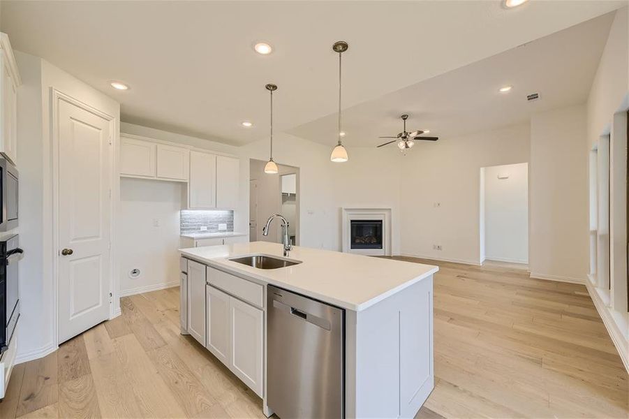 Kitchen with white cabinetry, light wood-type flooring, stainless steel appliances, a kitchen island with sink, and tasteful backsplash