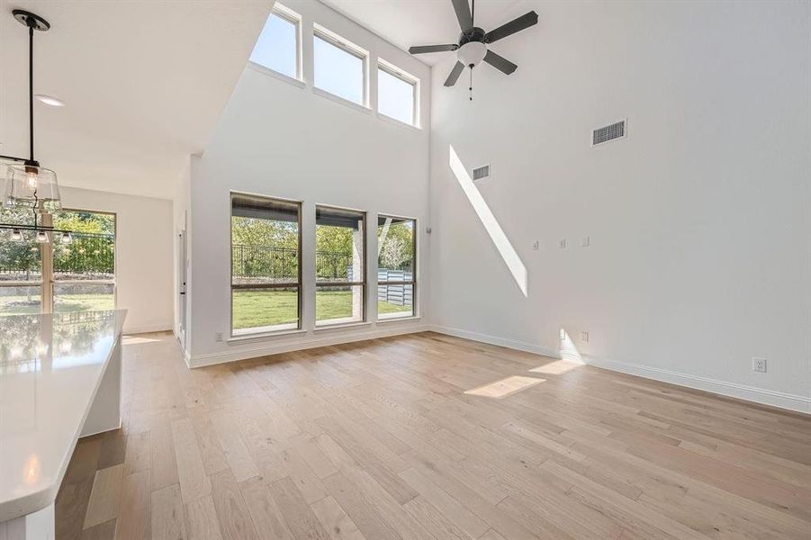Spacious living area featuring a vaulted ceiling, wood-finish flooring, a contemporary ceiling fan, and multiple windows providing views of the exterior landscape Spacious living area featuring a vaulted ceiling, wood-finish flooring, a contemporary ceiling fan, and multiple windows providing views of the exterior landscape