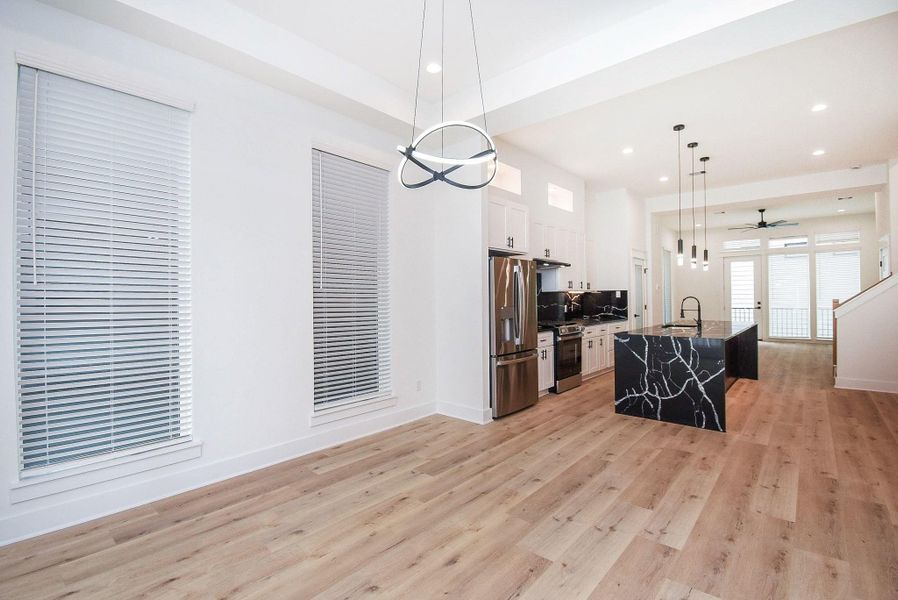 This modern, open-concept space features a sleek kitchen with stainless steel appliances, a striking black marble island, and ample natural light from large windows. The light wood flooring and contemporary lighting fixtures create a bright, inviting atmosphere, perfect for entertaining.